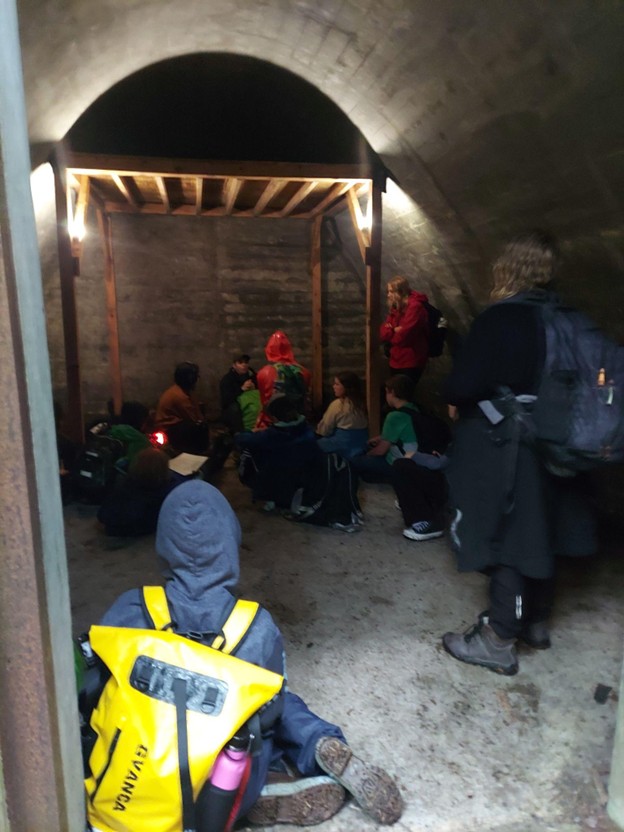 Camp kids seated on the floor of War Reserve Magazine B bunker at Fort McGilvray, listening to a lecture by the volunteer guide, Kendra Warlow
