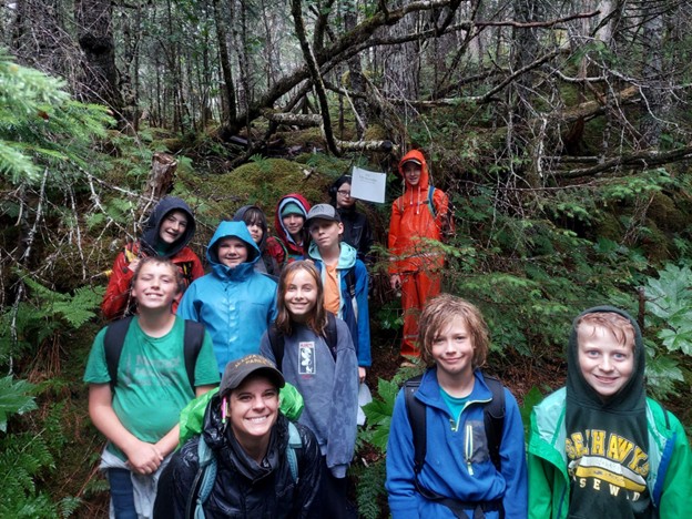 Camp kids clad in rain gear and wet from the rain posing for a photo on the Fort Trail No. 1 in Caines Head State Recreation Area